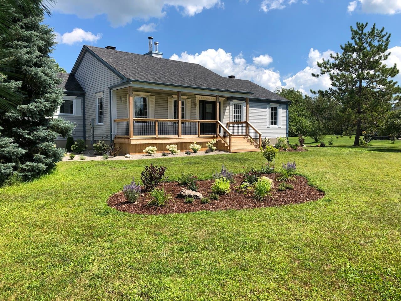 A new cedar front porch with wood railings and a fresh garden bed in front of a blue-grey house.