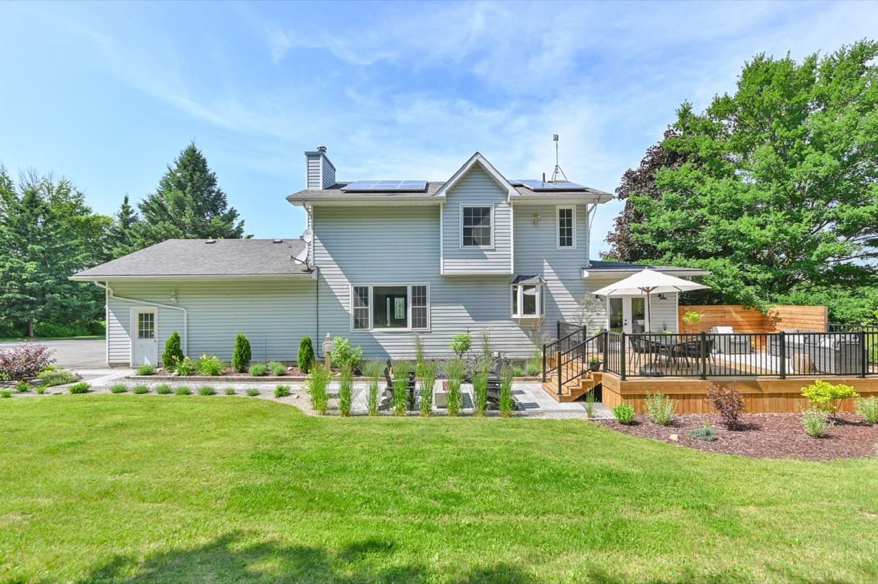 A large multi-level backyard deck with black railings and landscaped garden beds beside a grey two-storey house.